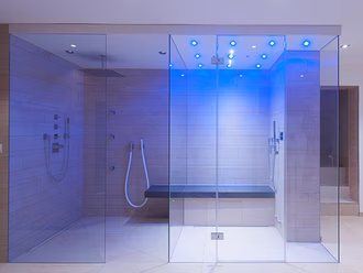 grosse-dampfdusche-viel-glas-farblicht-sitzbank-helle-fliesen-blau-beleuchtet-regenbrause
